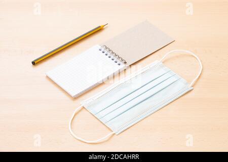 A face mask and a blank spiral notepad with a pen are arranged on a wooden table. To-do list concept during the Covid-19 Outbreak. Stock Photo