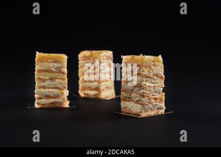 Three square pieces of white and yellow creamy cake, sweet delicious dessert isolated on black background. Tasty light mousse with apples, glazed on top. Concept of sweet desserts.