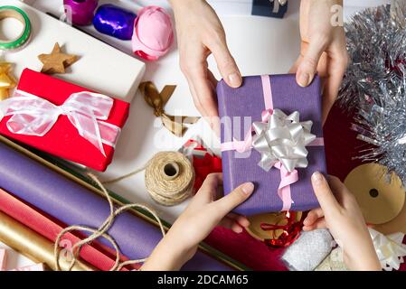 Female hands holding a small gift box wrapped in packing paper. To give and receive gifts from loved ones for christmas, valentines, birthday. Stock Photo