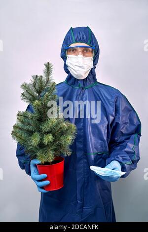 a man in a protective suit and mask with a Christmas tree in one hand and masks in the other hand Stock Photo