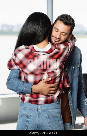 cheerful man smiling while hugging african american woman in airport Stock Photo