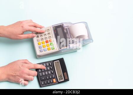 Close-up of a female hand pressing a finger on a cash register button and a hand pressing a button on a calculator on a blue background, top view, cop Stock Photo