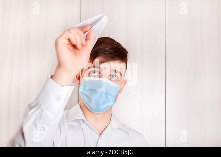 Young Man in Flu Mask with a Paper Plane by the Wall in the Room Stock Photo