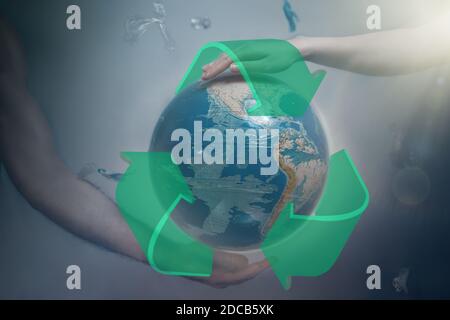 Women's and men's hands support the globe of planet Earth with sign of recycle. Around the flying plastic debris. The concept of preserving the earth' Stock Photo