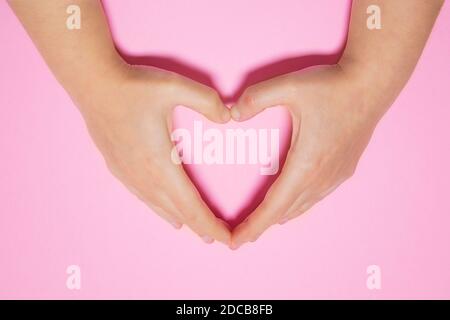 Close-up of a woman's hands drawing a heart on a pink background. Love and Valentine concept. Stock Photo