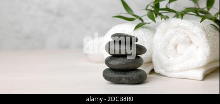 spa and wellness center - stack of massage stones and towels with green plant on white wooden table. banner copy space Stock Photo