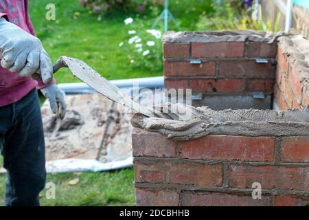 close up of bricklayer laying bricks with bricklaying trowel and mortar building a barbecue outside in summer Stock Photo
