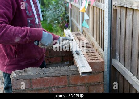 close up of bricklayer hand laying bricks and levelling up brickwork, building a barbecue outside in autumn Stock Photo