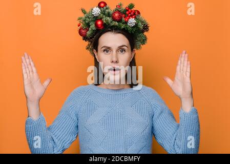 Stunned emotional young woman shapes very big object, impressed by huge size, gasps from wonder, wears in Christmas wreath and winter sweater Stock Photo