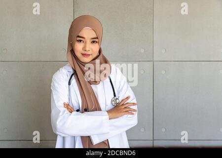 Confident Muslim female woman medical doctor standing and crossing arms with stethoscope; looking at camera Stock Photo