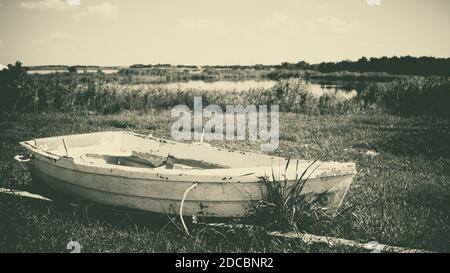 A beautiful grayscale shot of an old weathered fishing boat on a grassy shoreline Stock Photo