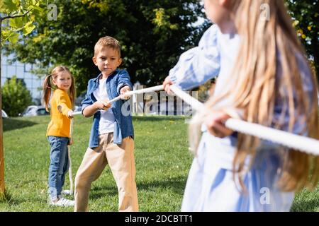 Boy pulling rope while playing tug of war with friends on blurred foreground in park Stock Photo