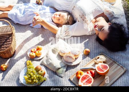 young pretty pregnant brunette woman having fun with her daughter on picnic on green grass in park, lifestyle people concept Stock Photo