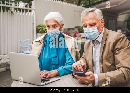 Beautiful senior couple with laptop computer sitting in a bar restaurant, communicating with family on a video call - concepts about elderly, lifestyl Stock Photo