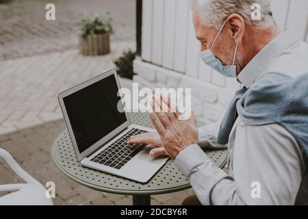 Cheerful senior man portrait with face mask during covid pandemic - Mature adult using his computer laptop in a bar coffeehouse, concepts about lifest Stock Photo