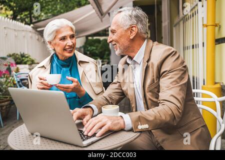 Beautiful senior couple dating outdoors - Mature couple with laptop computer sitting in a bar restaurant, concepts about elderly, lifestyle and techno Stock Photo