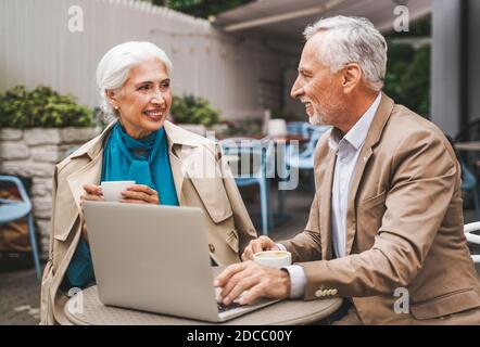 Beautiful senior couple dating outdoors - Mature couple with laptop computer sitting in a bar restaurant, concepts about elderly, lifestyle and techno Stock Photo