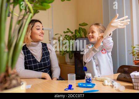 Little girl playing pretends like paediatrician doctor examining a patient in comfortabe medical office. Healthcare, childhood, medicine, education concept. Having fun while wearing gloves Stock Photo