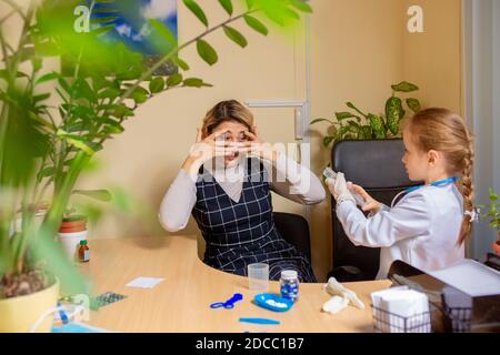 Little girl playing pretends like paediatrician doctor examining a patient in comfortabe medical office. Healthcare, childhood, medicine, education concept. Having fun while giving drugs Stock Photo