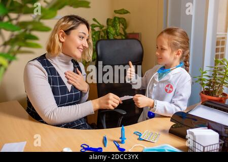 Little girl playing pretends like paediatrician doctor examining a patient in comfortabe medical office. Healthcare, childhood, medicine, education concept. Thankful patient shaking hand Stock Photo