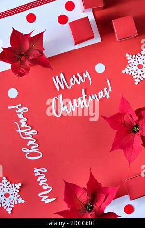 Text Merry Christmas. Poinsettia, snowflakes, red white paper confetti. Top view, monochrome design. Stock Photo