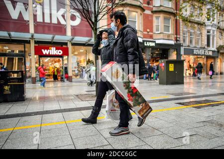 A man carries a Christmas tree in the centre of Cardiff where shops are open and people are out in numbers taking advantage of buying nonessential items in the run-up to Christmas. Restrictions across Wales have been relaxed following a two-week 'firebreak' lockdown. Stock Photo