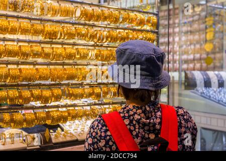 A Chinese woman wearing a hat and watching the golden jewelry at the gold street, also called Gold souk, in the city of Dubai, UAE Stock Photo