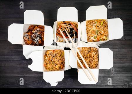 top view of chinese fast food in disposable cardboard boxes and wooden chopsticks on black table Stock Photo