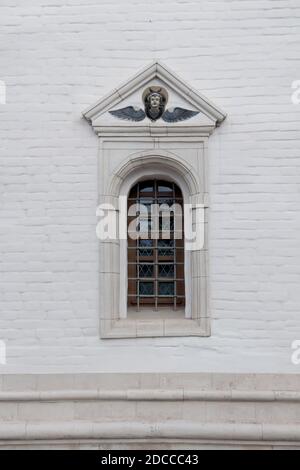 Old arched window with metall lattice and relief on a white brick wall of christian church Stock Photo