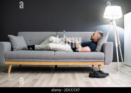 Man Lying In Sofa At Home And Using Laptop Stock Photo