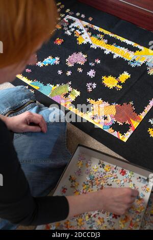 A woman with red hair kneeling on the floor doing a colourful jigsaw puzzle Stock Photo