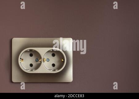Golden double power socket on a painted brown wall. Standard european electrical connector close-up Stock Photo