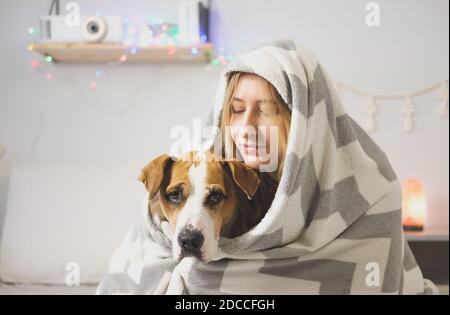 Portrait of a smiling woman hugging her staffordshire terrier dog, wrapped in blanket. Joy from pets at home or during lockdown or self isolation, col