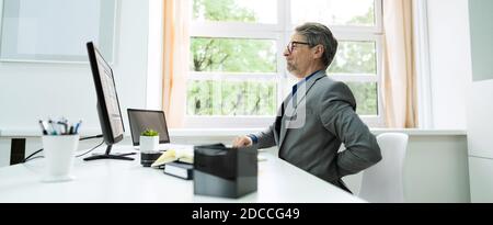 Businessman Having Back Pain While Sitting At Office Desk Stock Photo