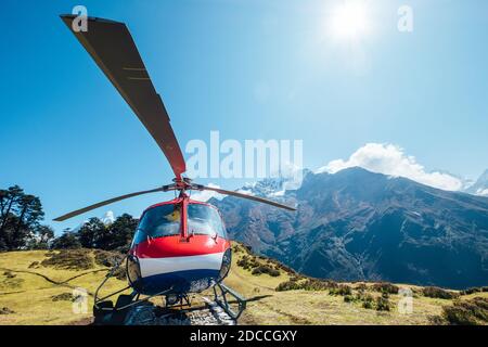 Civil helicopter landed in high altitude Himalayas mountains. Thamserku 6608m mountain on the background. Namche Bazaar, Nepal. Safety air transportat Stock Photo