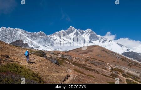Alone Young backpacker woman with trekking poles going to Lhotse Base Camp. Dangerous Lhotse South Face with summit 8516m and blue sky on background. Stock Photo