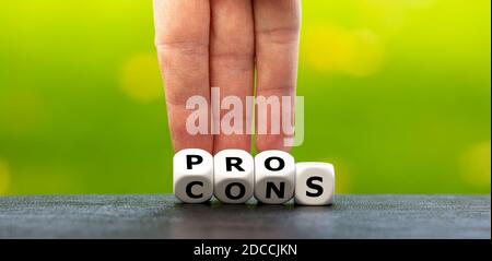 Hand turns dice and changes the expression "cons" to "pros". Stock Photo