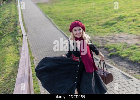 walks up the stairs and in a burgundy palette and biret, with a beautiful smile in black clothes, in the fall against the blue sky. Stock Photo