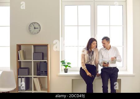 Man and woman office workers analyze documents standing in the office by the window. Stock Photo