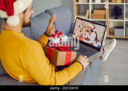 Young man sitting on couch with laptop and video calling his girlfriend on Christmas holidays Stock Photo