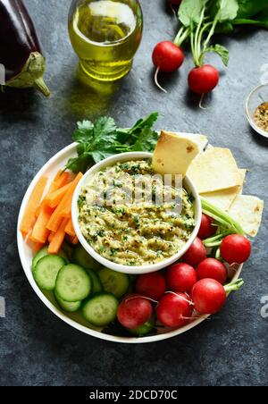 Baba ganoush (roasted eggplant dip) in bowl and fresh organic vegetables over blue stone background. Healthy eating. Vegetarian vegan food concept. Stock Photo