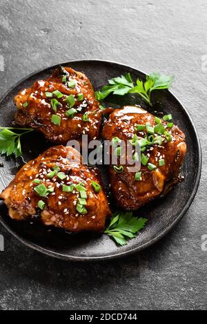 Sweet and spicy honey grilled chicken thighs on plate over dark stone background. Tasty food in asian style. Stock Photo
