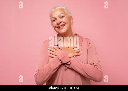 Senior woman keep getting compliments. Delighted happy charming old lady with white hair smiling at camera. Studio shot on pink wall. Stock Photo