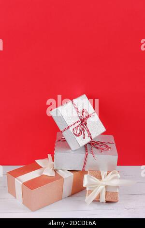 Pile of shining silver and golden gift boxes wrapped in ribbon on a wooden white table with red background. Holiday concept with upper copy space. Chr Stock Photo