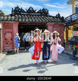 Three Vietnamese young ladies in traditional dress, the ao dai, posing for a photograph at the Japanese covered bridge, Hoi An, Vietnam, Asia