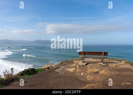 A scenic viewpoint with wooden bench on beautiful ocean coast with high cliffs and big waves Stock Photo