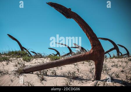 Anchor's cementary on the beach at Praia Do Barril in Santa Luzia, Algarve, Portugal. Old rusty marine anchors in dunes with blue sky. Stock Photo