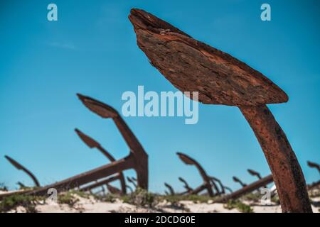 Anchor's cementary on the beach at Praia Do Barril in Santa Luzia, Algarve, Portugal. Old rusty marine anchors in dunes with blue sky. Stock Photo
