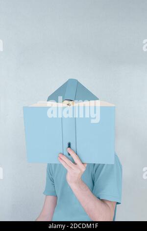An abstract portrait of a young man reading covering his head and face with two books on a blue background. Stock Photo