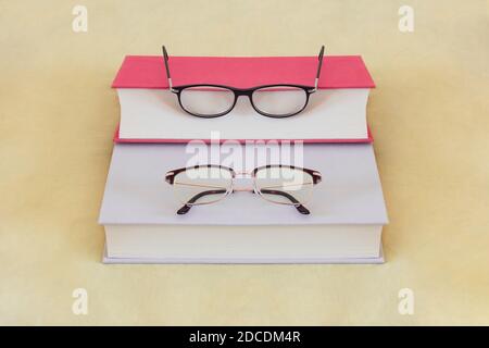 A couple's glasses rest on two thick hardcover books of different colors on top of a mattress with yellow sheets. Read and learn together concept. Stock Photo